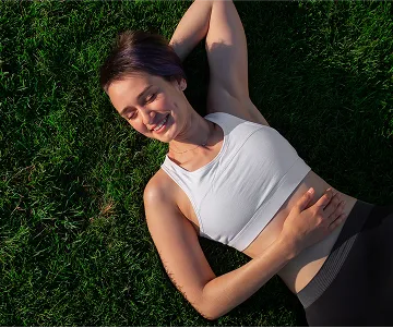 Happy young woman enjoying relaxation outdoors, lying comfortably on fresh green grass under warm sunlight, promoting self-care, stress relief, and a healthy active lifestyle