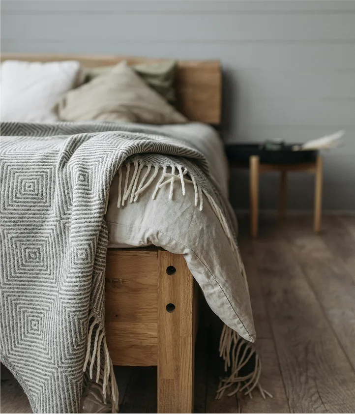 Cozy bed with gray blanket, soft pillows, and side table