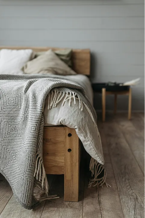 Cozy bed with gray blanket, soft pillows, and side table