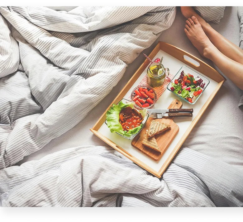 Cozy unmade bed with rumpled linens, bird art on wall, and bedside lamp