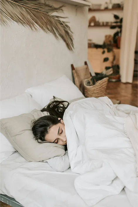 Person peacefully asleep on cozy bed with white linens in a serene, stylish bedroom.
