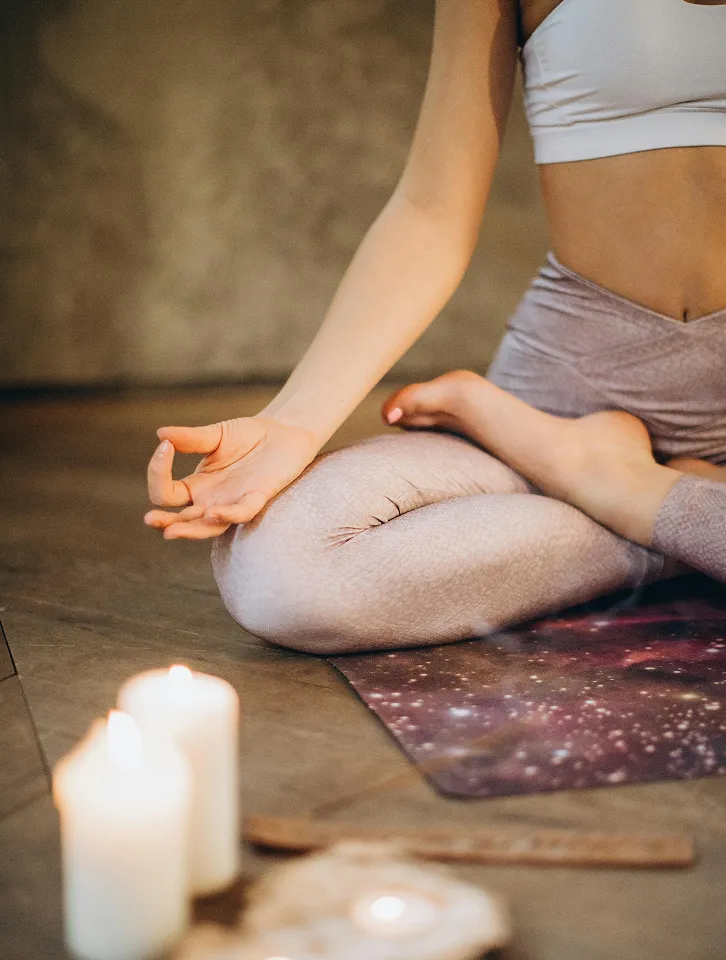 Woman in yoga attire meditating with peaceful hand gesture, surrounded by lit candles.