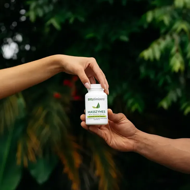 handing a Masszymes bottle to another in a green setting