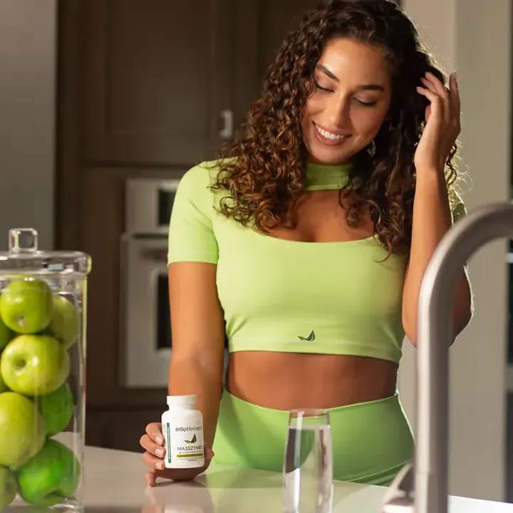 Person in green outfit holding supplement bottle in kitchen