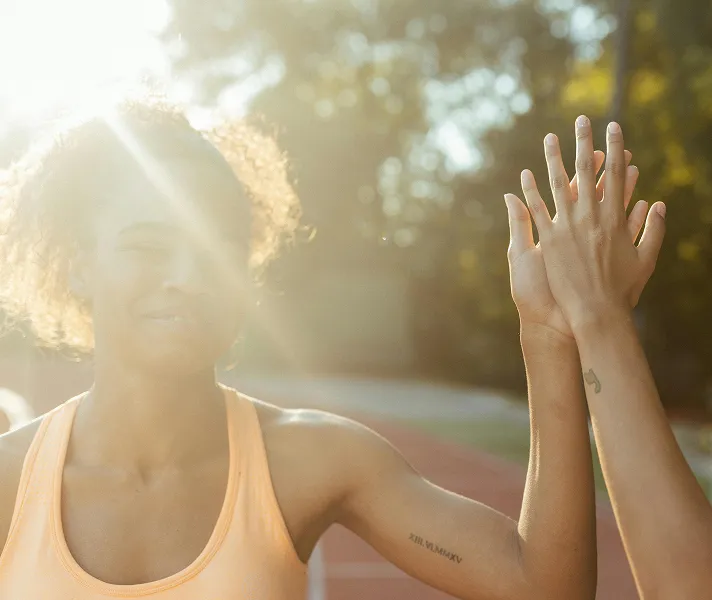 Two people holding hands on a sunlit track field