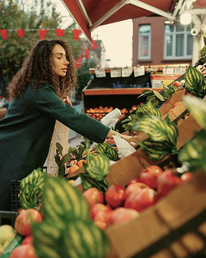 Woman in green coat picking apples at outdoor market