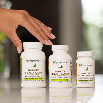 a close up of a womans hand reaching for three bottles of probiotic breakthrough