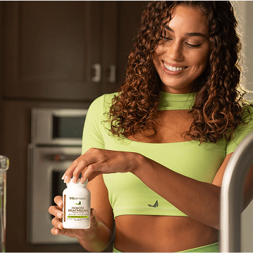 a woman in a green top holds a supplement bottle 