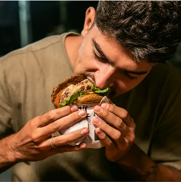 person holding a wrapped burger with garnishes