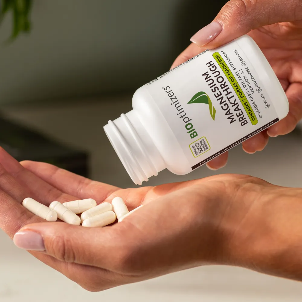 Hand holding several white Magnesium Breakthrough capsules poured from a BIOptimizers supplement bottle
