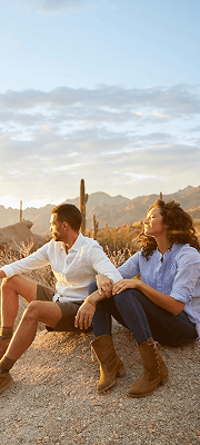 Couple sitting on desert rocks at sunset with mountain and cactus landscape in the background