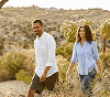 Couple sitting on desert rocks at sunset with mountain and cactus landscape in the background