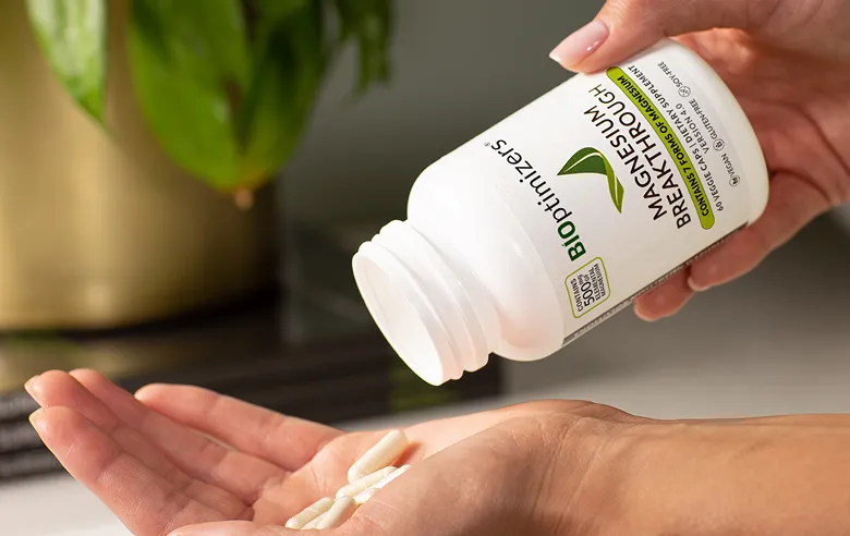Person pouring white magnesium supplements into their palm with a green plant in the background