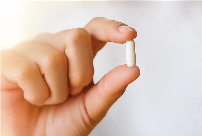 hand holding a small white capsule
